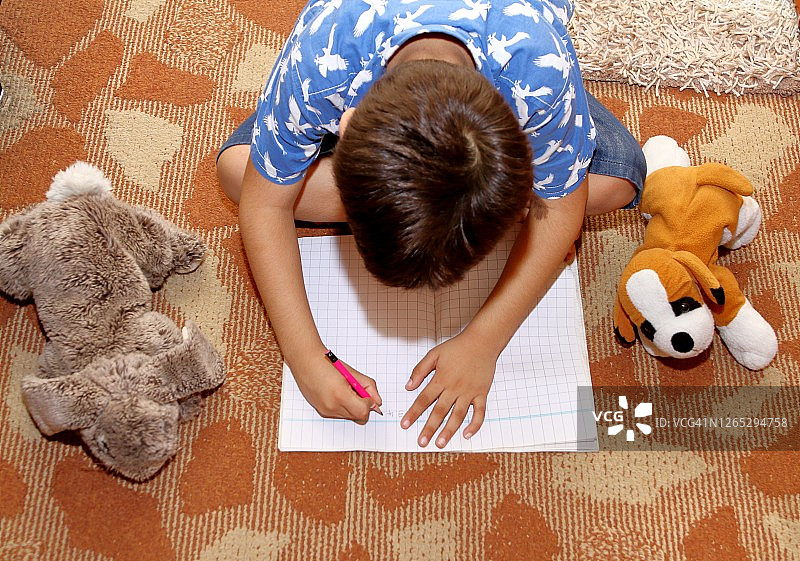 一个小男孩在笔记本上学习和写作的高角度视图。图片素材