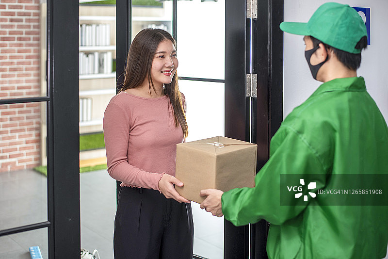快递员身着绿色制服将纸板箱包裹给收货人，新常态的生活理念。图片素材