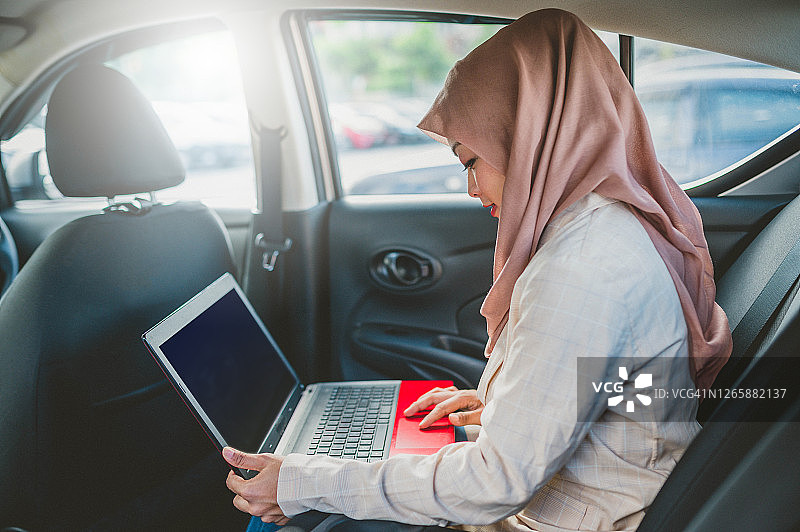 年轻的亚洲穆斯林女企业家坐在车里，拿着笔记本电脑图片素材