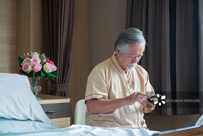 年长的亚洲病人正在用手机支付商品、服务或交流。图片素材