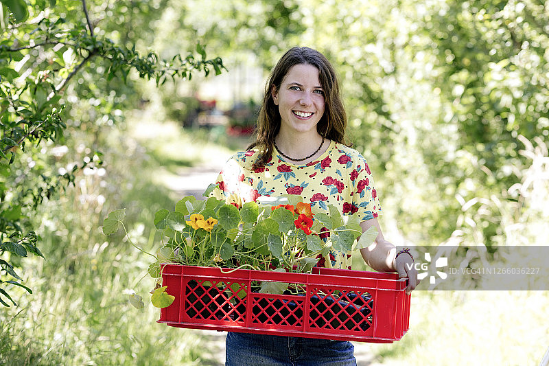 微笑的年轻女子提着篮子里的旱金莲在农场图片素材