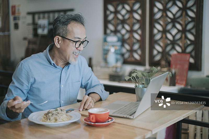 一位亚洲华人长者在一家咖啡厅与同事通过网络虚拟会议进行讨论图片素材