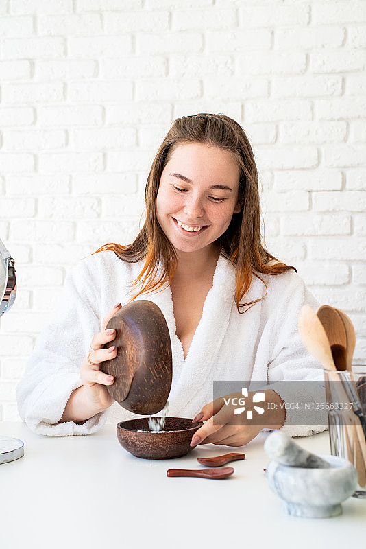 年轻微笑的白人妇女穿着浴衣做水疗程序使用天然化妆品图片素材
