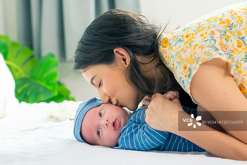 微笑美丽的白人母亲亲吻她的新生儿在床上的卧室。妈妈和可爱的男婴在家里一起休息放松。幸福家庭，宝宝保健理念。图片素材