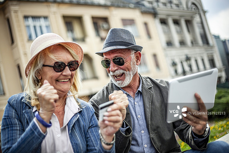 两个老人在网上购物用数字平板电脑-快乐的老年夫妇坐在城市散步和网上购物图片素材
