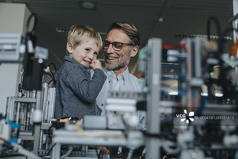 在工厂的实验室里，微笑的男科学家向儿子展示机器图片素材