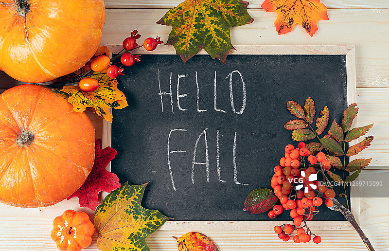 你好,秋天。南瓜，浆果和落叶与粉笔黑板框架在木制的背景。万圣节、感恩节或秋季季节。平躺，俯视图图片素材