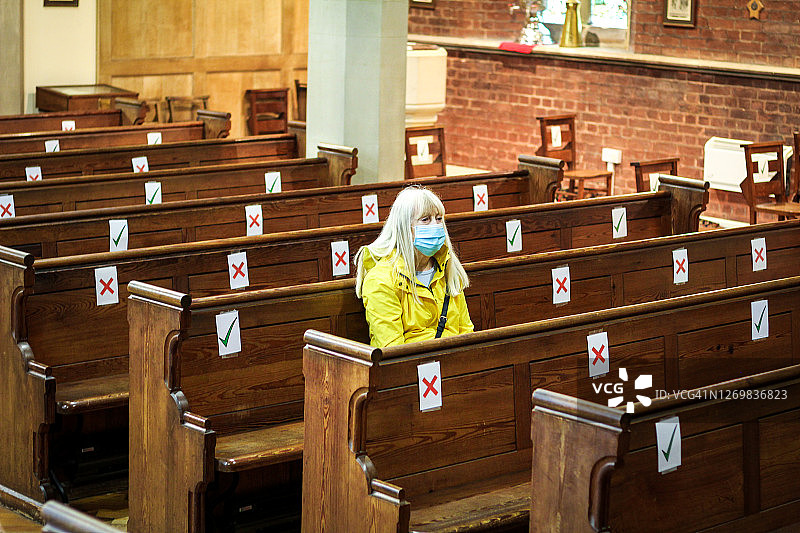 在教堂祈祷的年长妇女戴着防护面具图片素材