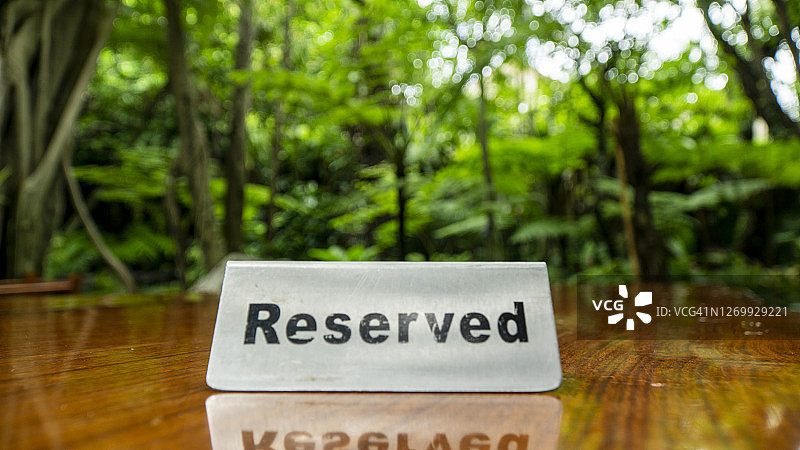 保留的标识由不锈钢板制成的压合木餐桌上的餐厅与树木和森林的背景。图片素材