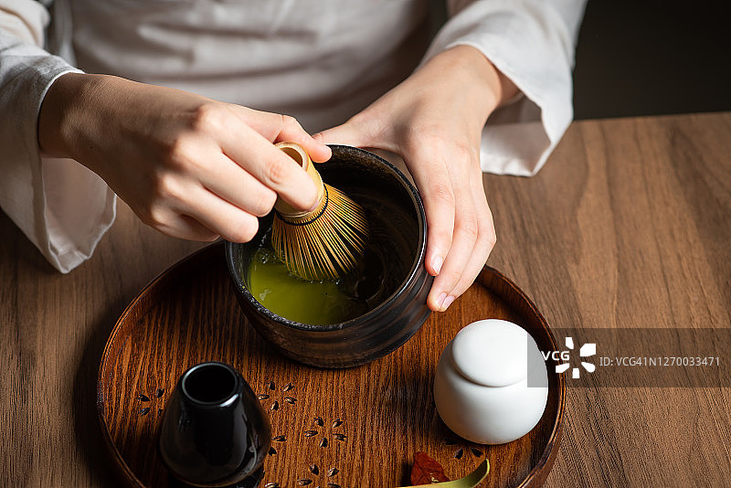 女士一边搅拌抹茶粉，一边用传统的茶道用具制作抹茶绿茶图片素材
