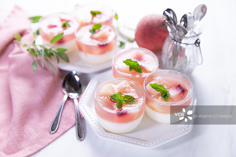 大理石背景上的玻璃罐中自制的意式奶冻和桃子片和桃子果冻。图片素材