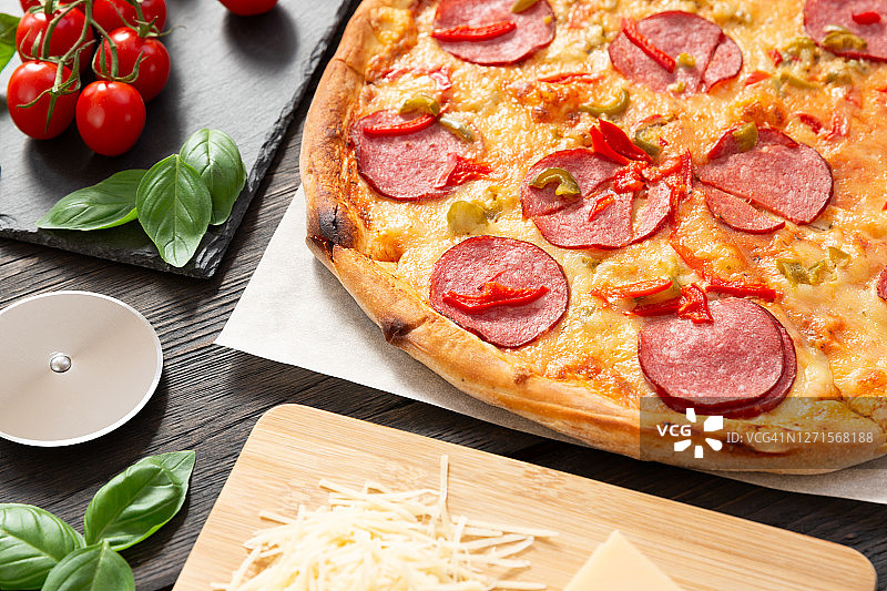 美味的热披萨配料和切披萨刀在黑色纹理的背景图片素材