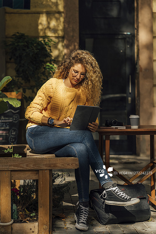 年轻的金发女人坐在城市路边的咖啡馆里使用着平板电脑图片素材