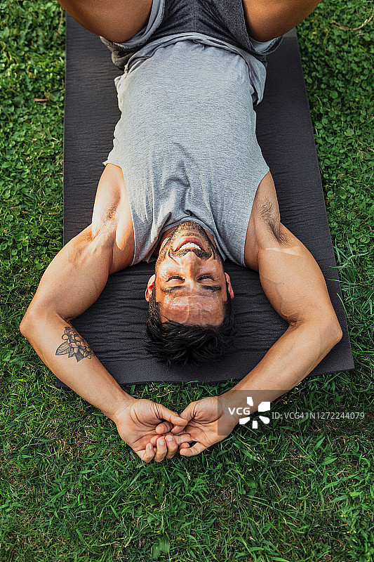 微笑的男人躺在公园的运动垫子上图片素材