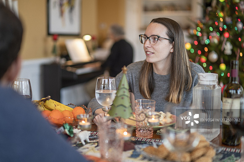 年轻的女人和她的丈夫正在吃饭，而年长的男人，也就是父亲，正在为圣诞节装饰的客厅里弹奏钢琴图片素材