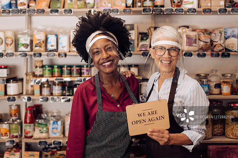 两名健康食品店女店主举着重新开业的牌子图片素材