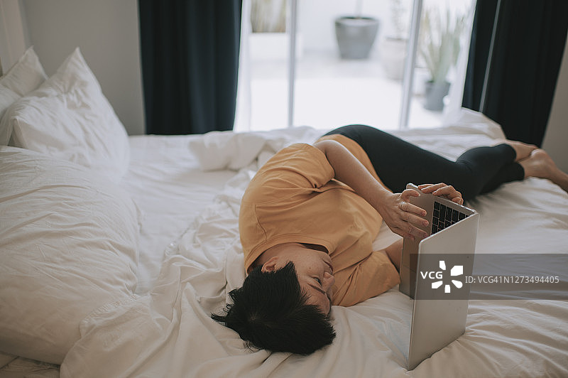 亚洲妇女在家工作，躺在床上使用笔记本电脑图片素材