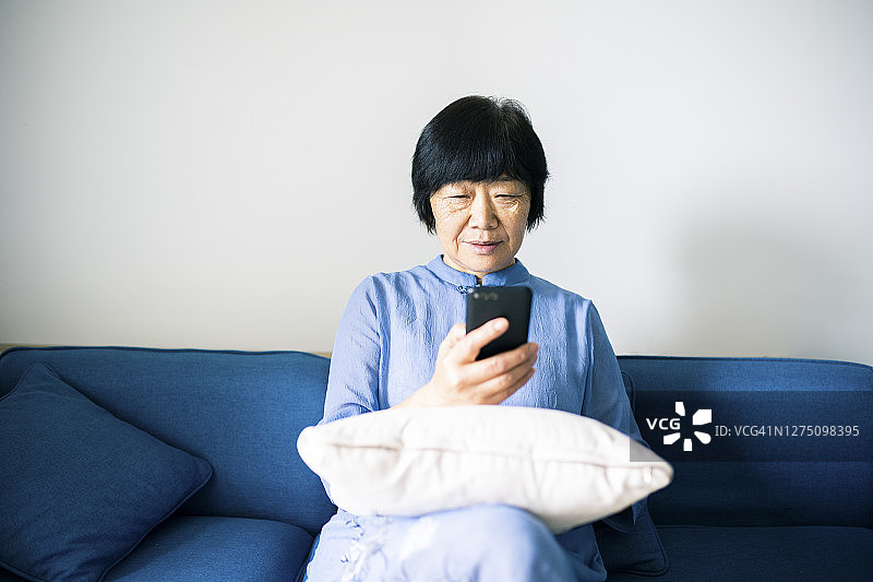在家里使用智能手机的资深亚洲女性图片素材