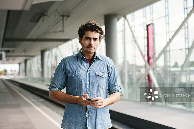 自信的休闲商人站在火车站平台上使用智能手机图片素材