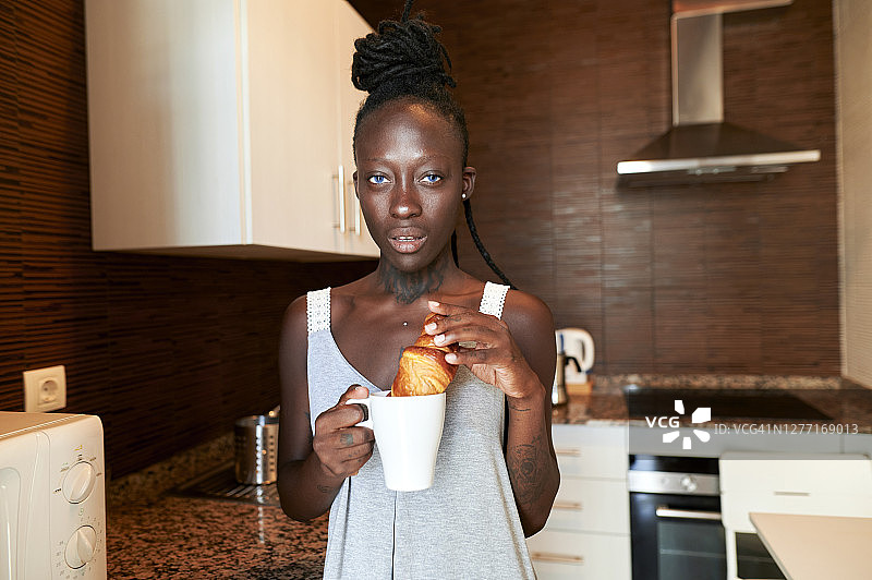 年轻女子在家里的厨房里吃牛角面包和咖啡图片素材