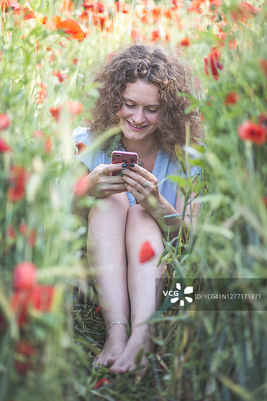 年轻女子坐在农田里使用手机图片素材