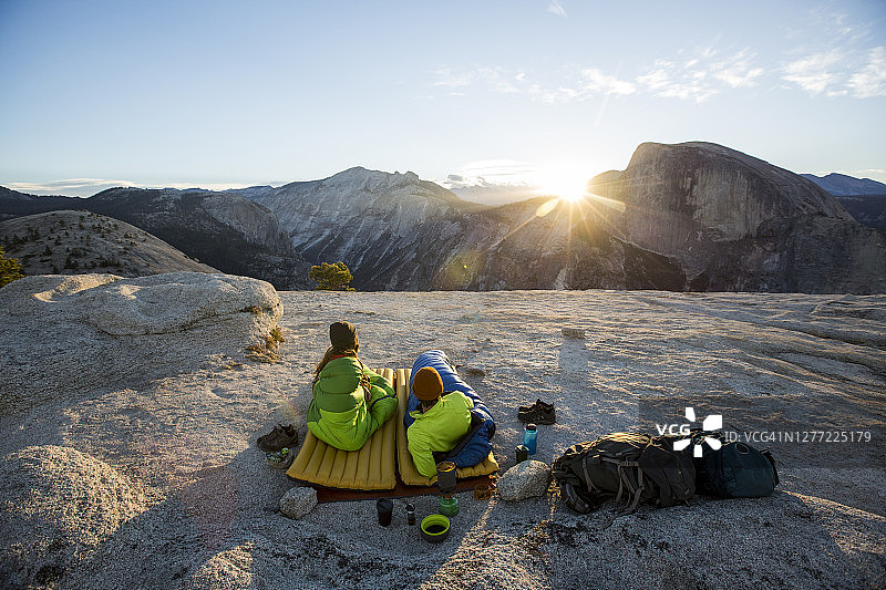 一对夫妇在半圆顶和远处的约塞米蒂山谷的一个岩石岬上露营。图片素材