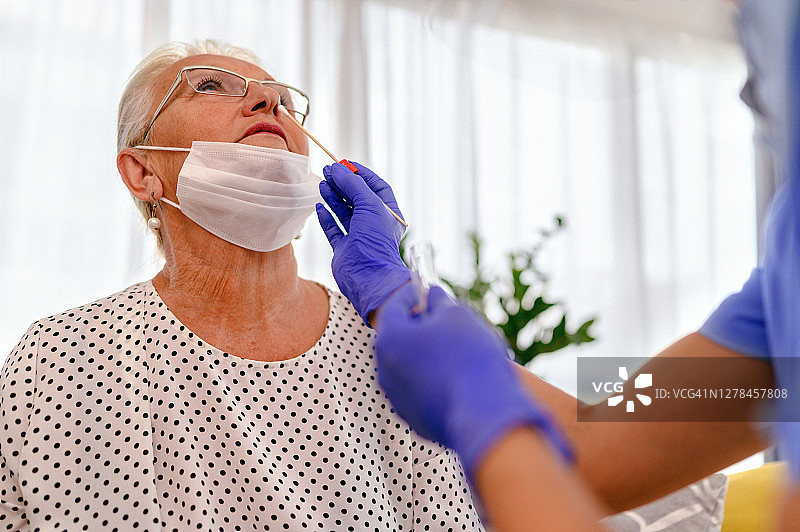 女医生为一名资深女性进行鼻拭子检测，以进行COVID-19检测图片素材