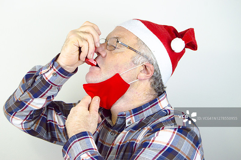 (2019冠状病毒病)戴有红色面罩的圣诞老人帽和使用哮喘吸入器的人图片素材