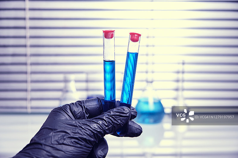 实验室员工戴着黑色医用手套，拿着一个装有蓝色液体的试管。病毒流行病和隔离图片素材