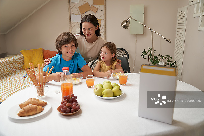 年轻美丽的白人家庭的肖像，母亲和她的两个可爱的孩子坐在厨房的桌子在家里和一起吃早餐图片素材