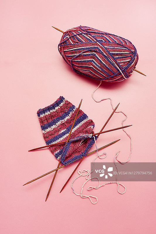 在粉红色的背景上编织袜子、针织针和毛线球图片素材