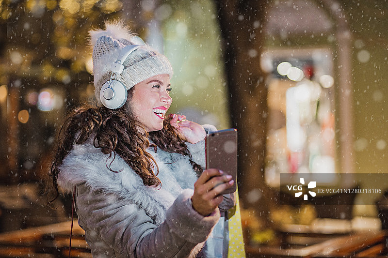 年轻女子在冬夜里拿着购物袋享受着音乐图片素材