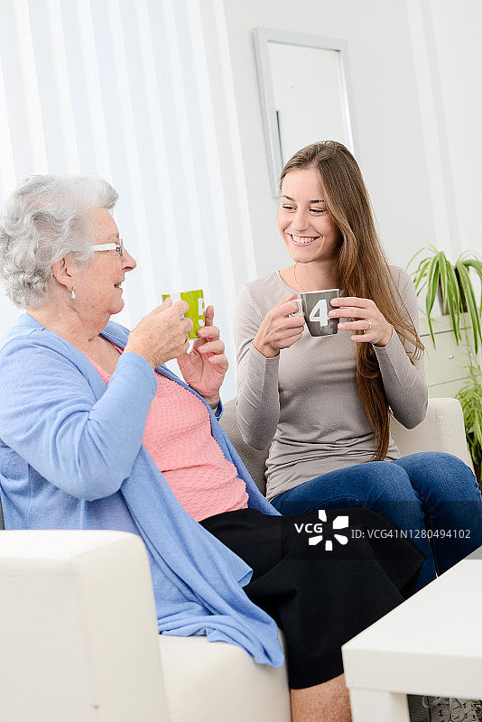 快乐的老女人花时间喝茶与愉快的年轻女孩在家里图片素材