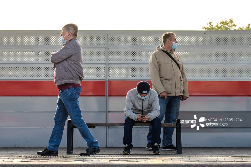 一群戴着医用防护口罩的男性乘客在火车站站台上等车。图片素材