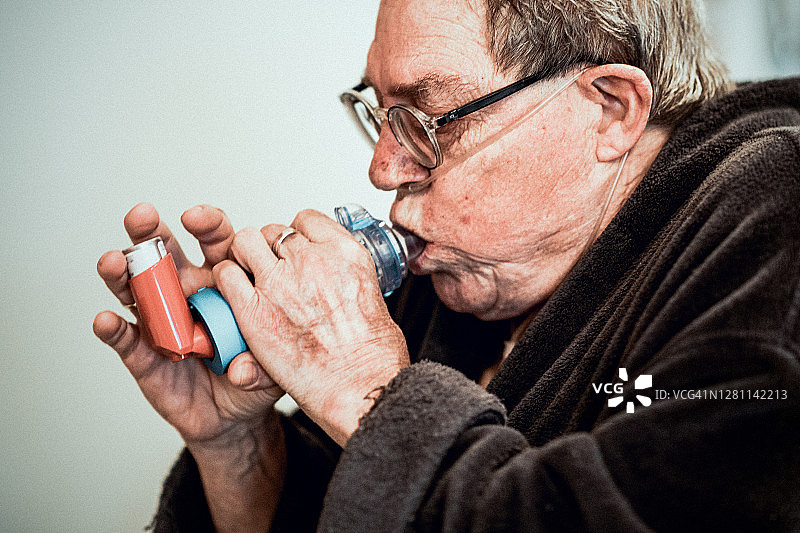 一位老人，站在他的厨房里，正在他的支气管扩张治疗吸入药物。图片素材