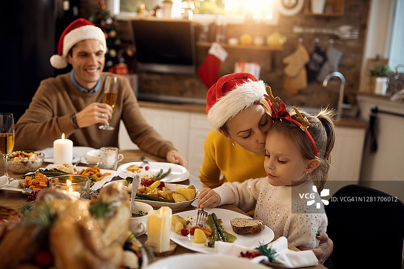 圣诞节那天，慈母在餐桌上与家人共进午餐时亲吻女儿。图片素材