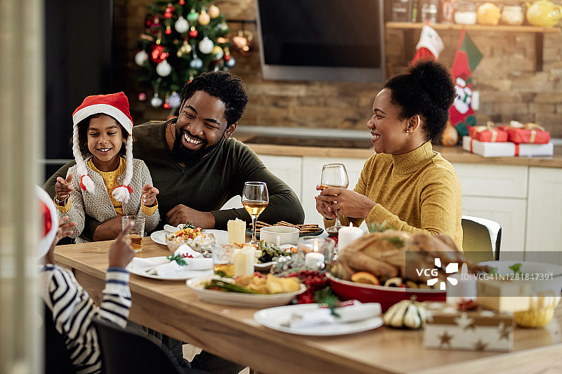 快乐的非裔美国家庭在圣诞午餐餐桌上聊天。图片素材