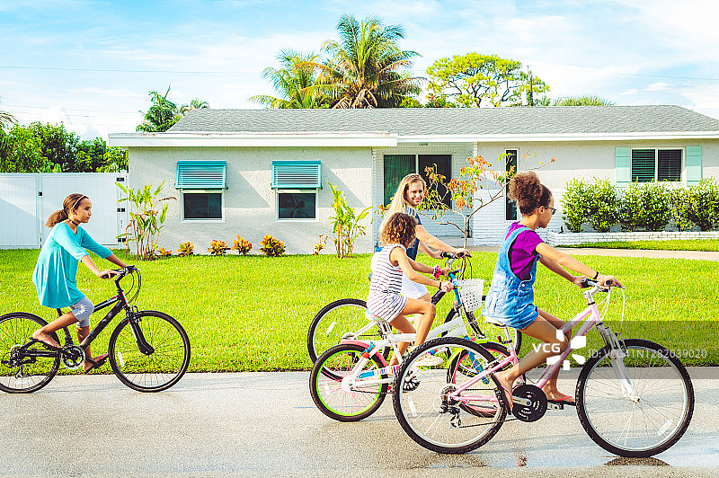 家庭骑自行车，母亲和混血女儿在郊区社区图片素材