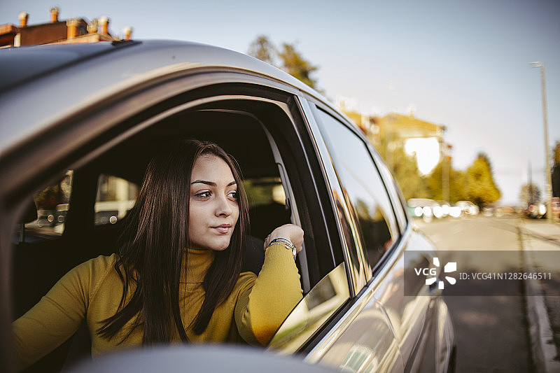 年轻的学生骄傲地坐在她的新车-快乐的司机驾驶一辆车-一个快乐的细心的司机女人驾驶一辆车在道路上的肖像图片素材