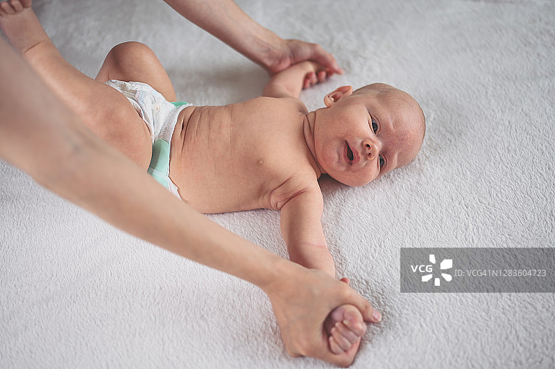 妈妈在给穿着尿布的宝宝做运动。可爱的情感的有趣的新生婴儿小男孩在婴儿床。图片素材