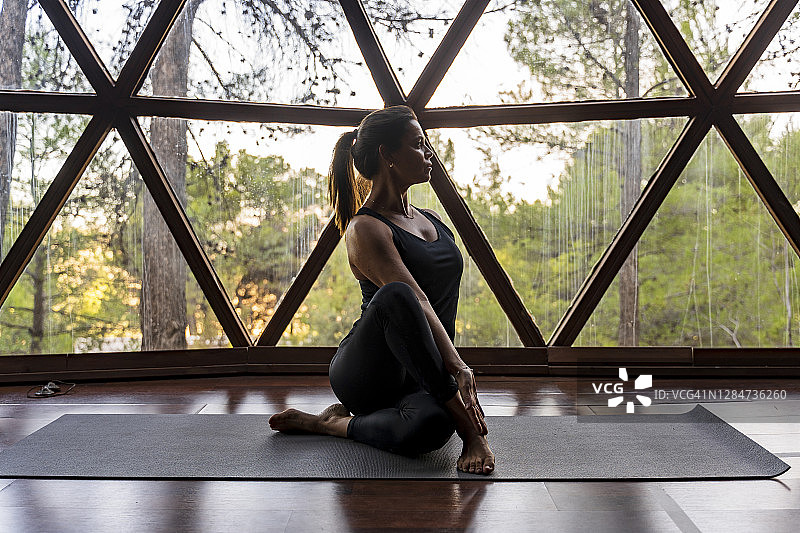 灵活的成熟女性教练在健身中心的垫子上对着窗户练习瑜伽图片素材