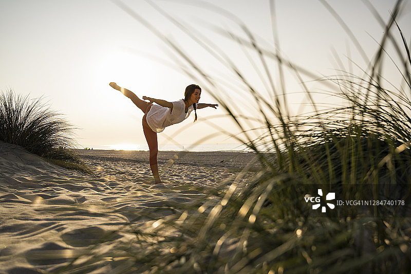 柔韧的年轻女子在日落时在沙滩上练习瑜伽图片素材