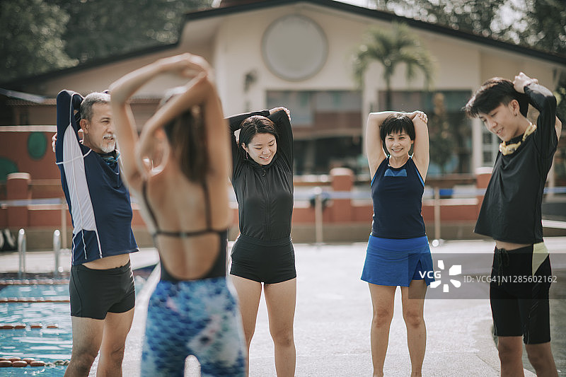 上午，亚洲华人家庭跟着教练在游泳池做热身运动图片素材