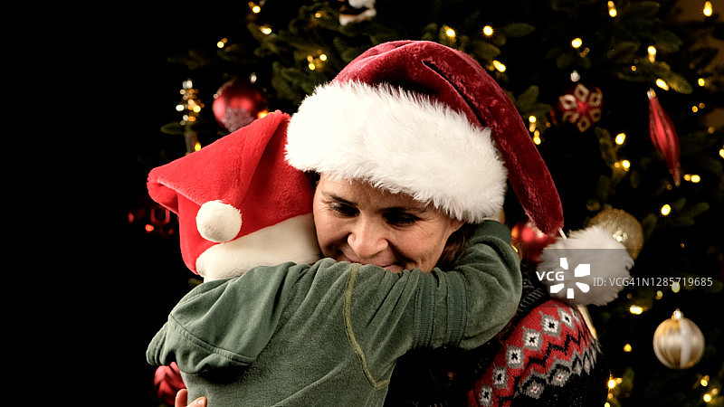 微笑成熟的女人和她的儿子拥抱在圣诞树旁图片素材