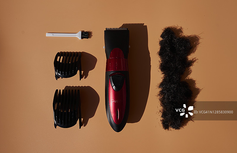 切割机配备有切割机、梳子、刷子和棕色背景上的天然黑色人类头发。水平的照片图片素材