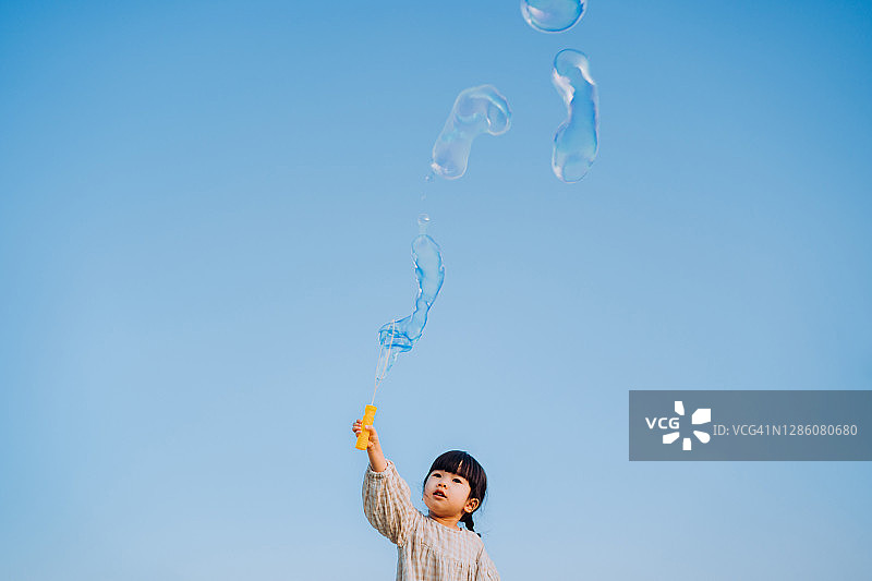 可爱的亚洲小女孩拿着泡泡棒玩肥皂泡户外在自然公园对抗美丽的蓝天在一个可爱的日子图片素材