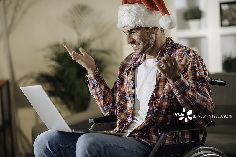 一个年轻人坐在轮椅上与圣诞老人的帽子在一个视频电话祝愿圣诞股票照片快乐图片素材