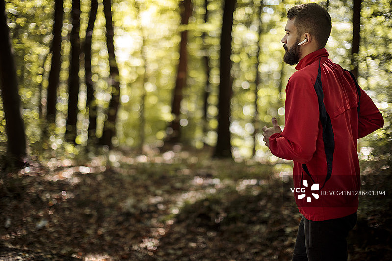 年轻的运动员戴着蓝牙耳机在森林里慢跑图片素材