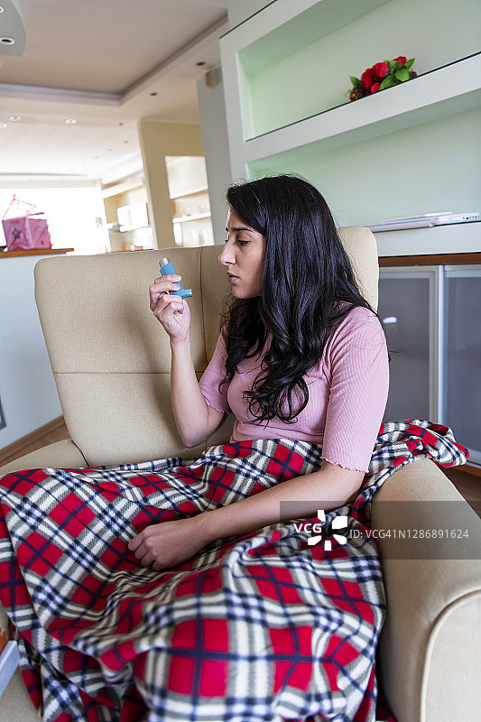年轻女子在家里使用哮喘吸入器图片素材