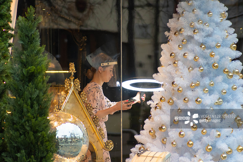 美丽的年轻白人女孩戴着塑料保护面罩和装饰圣诞树在商店图片素材
